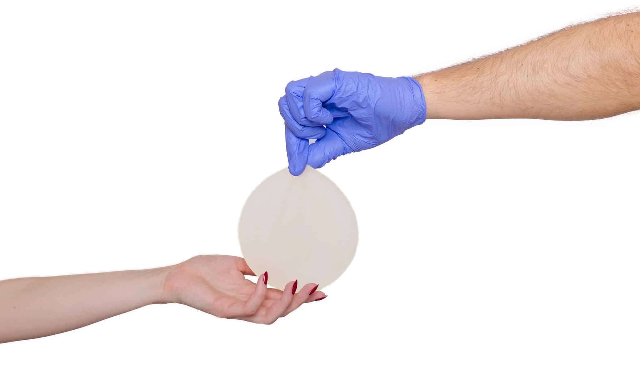 Gloved hand holding breast implant over another hand.
